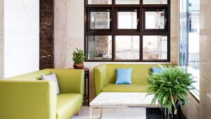 Eine moderne Lobby mit einem grünen Sofa, einem Marmortisch und großen Fenstern mit Blick auf die Stadt.