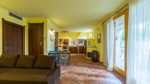 Un salon avec un canapé, une table à manger avec des chaises, une cuisine en arrière-plan et une porte-fenêtre coulissante donnant sur un espace extérieur.