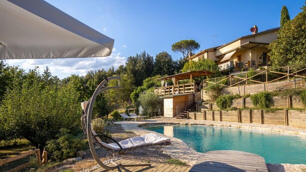Un espace piscine doté d’une terrasse en bois, de chaises longues et d’un coin salon abrité.