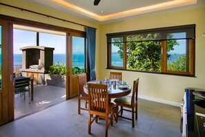 A dining area with a round table and chairs, a stone fireplace, and large windows offering ocean views. - Ocean View Luxury Bed Villa with lovely Infinity Pool, FREE CAR & Free Transfers (Koh Samui)