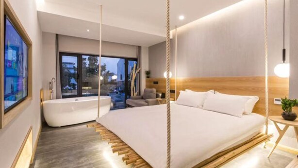 A modern bedroom with a large bed, a bathtub, and a view of the city. - Suzhou Jianluju Inn (Suzhou)