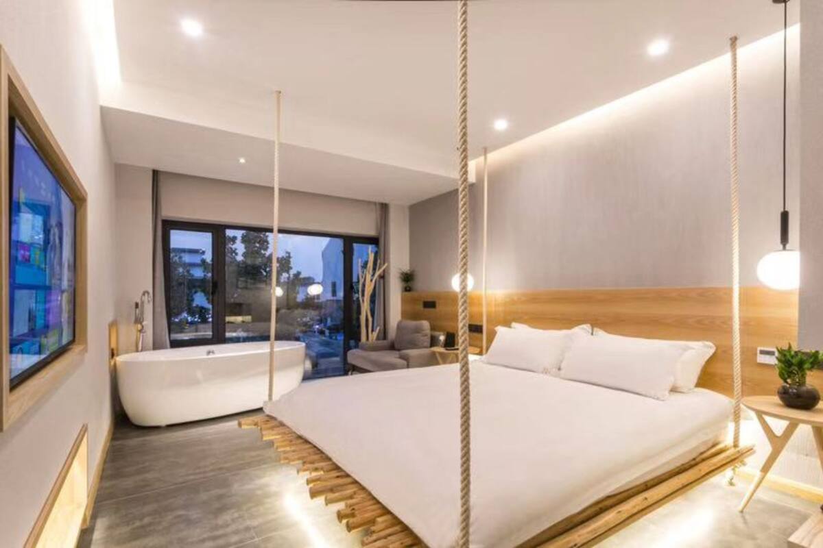 A modern bedroom with a large bed, a bathtub, and a view of the city.