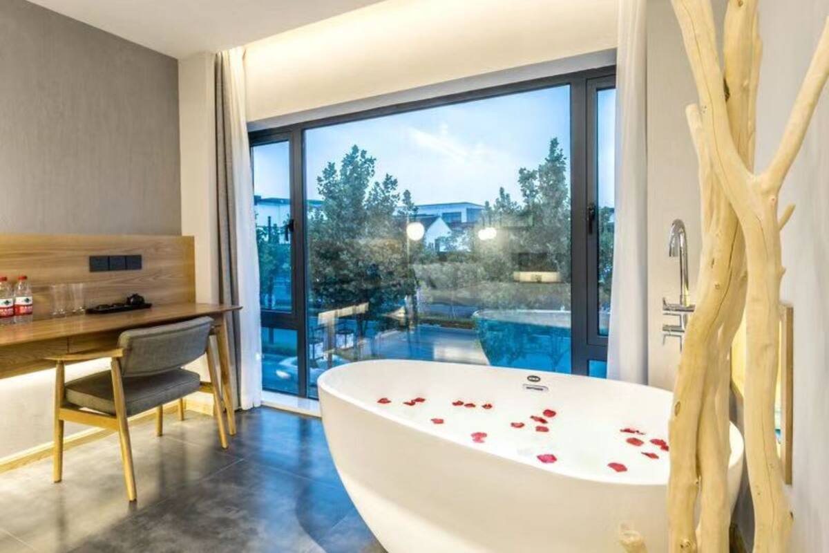 A modern bathroom with a freestanding bathtub, a wooden desk, and a chair.