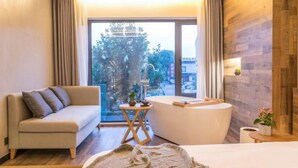 A modern hotel room with a sofa, a small round table, a bathtub, and a view of the city through large windows. - Suzhou Jianluju Inn (Suzhou)