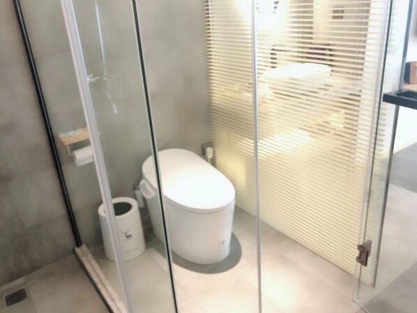 Une salle de bain moderne avec une paroi en verre, des toilettes et une poubelle.