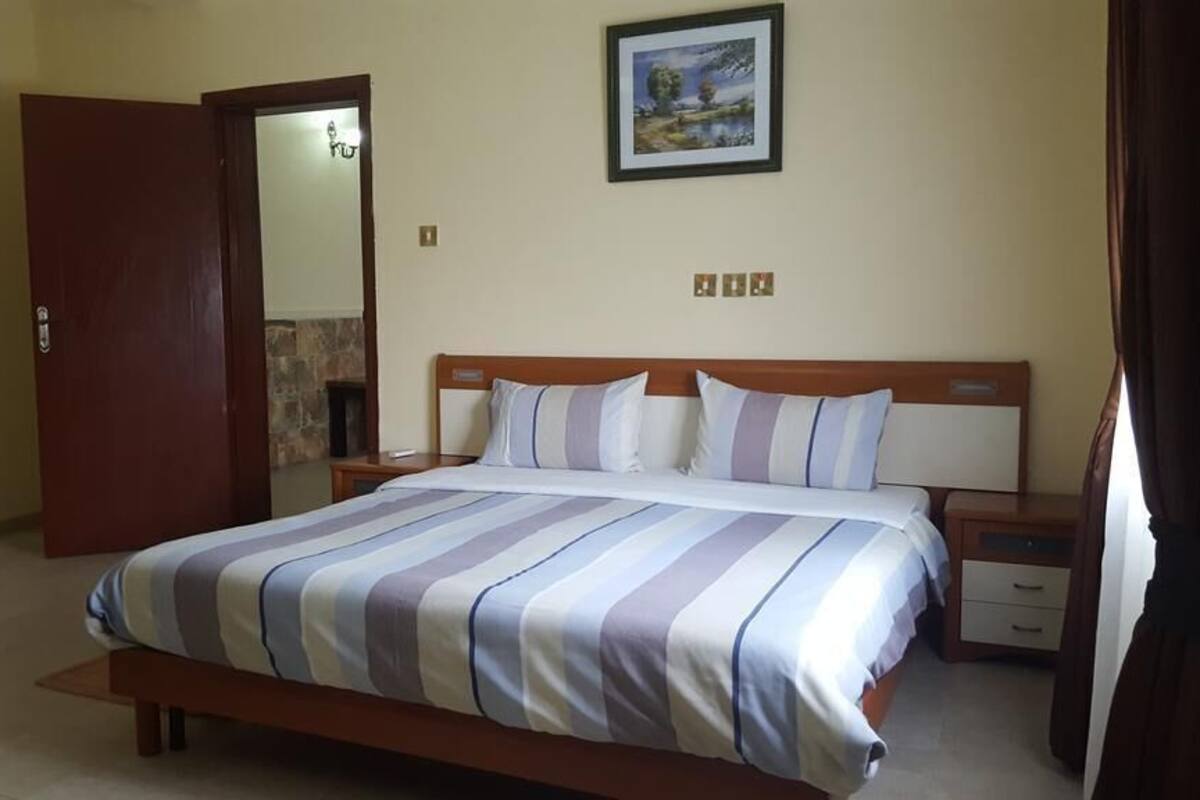 A bedroom with a bed, a nightstand, a wooden headboard, a painting on the wall, and a door.