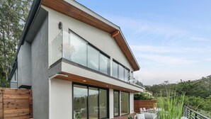 A modern two-story house with a large glass balcony, wooden deck, and outdoor seating area. - Exceptional Hilltop Villa with Panoramic View (SF)