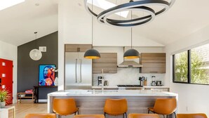 A modern kitchen with a central island, pendant lights, and a dining area with orange chairs. - Exceptional Hilltop Villa with Panoramic View (SF)