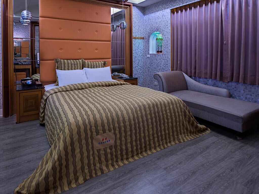 A bedroom with a large bed, a sofa, a nightstand, and a mirror.