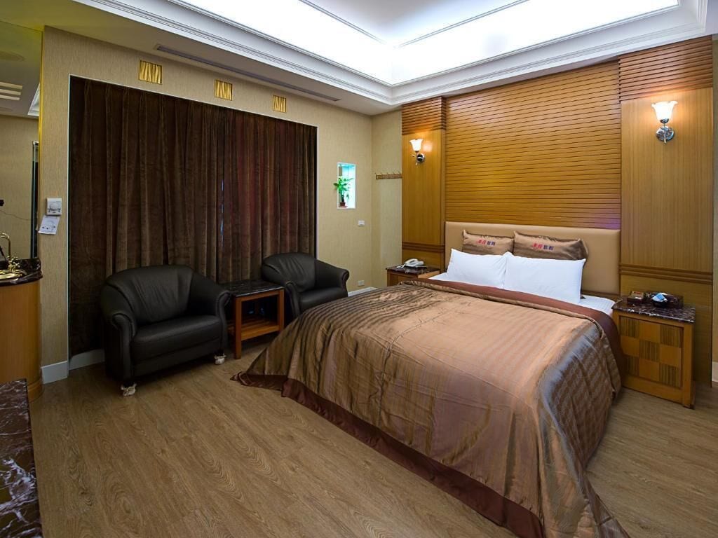 A hotel room with a large bed, a sofa, a desk, and a wooden headboard.