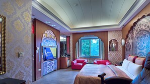 Een ruime slaapkamer met een groot bed, een kaptafel met spiegel en een raam met uitzicht op bomen.