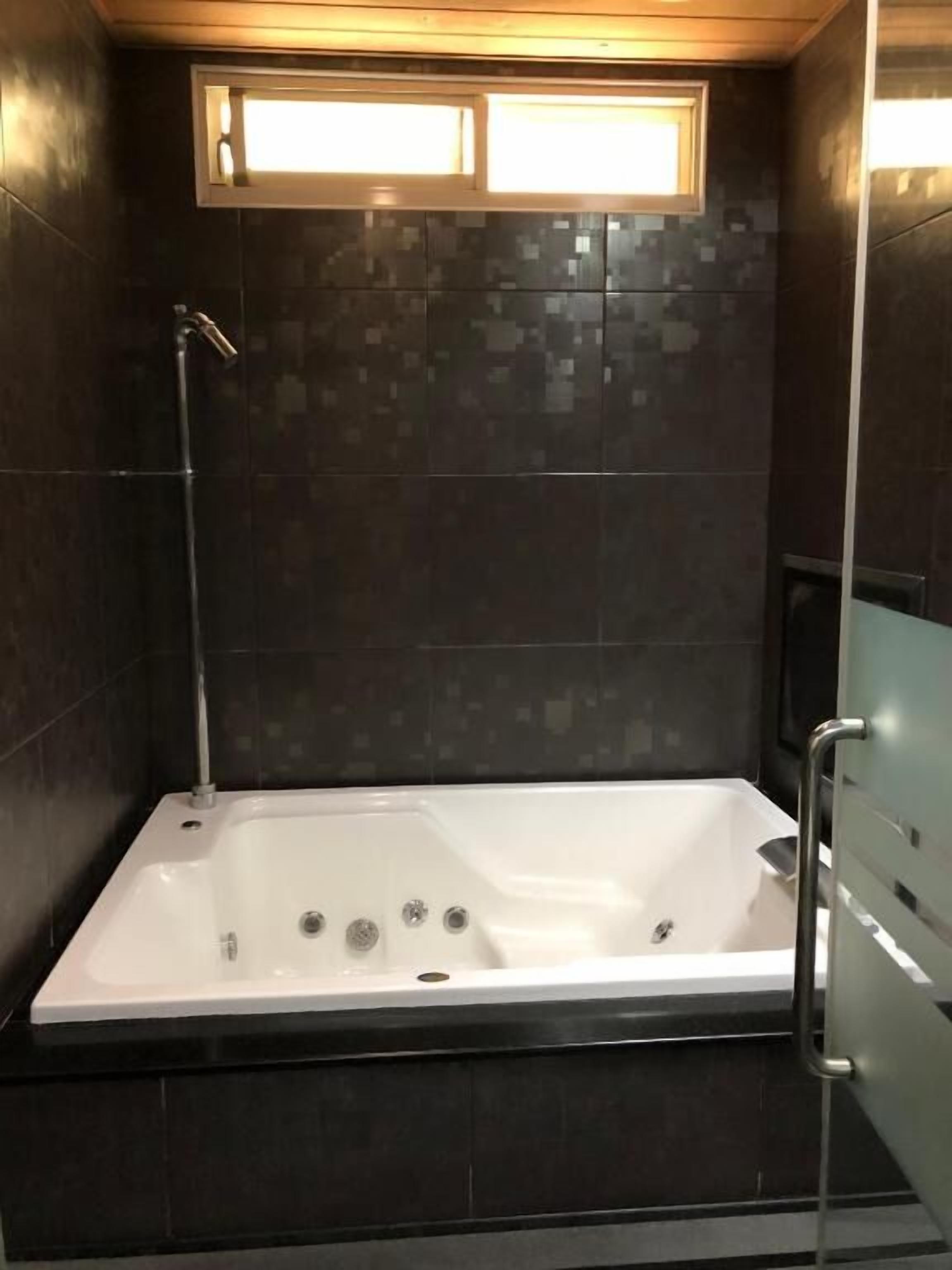 A modern bathroom with a walk-in shower, dark tiled walls, and a window above the bathtub.