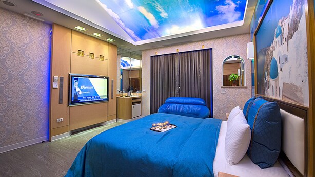 Een hotelkamer met een groot bed, een televisie, een bureau met een computer en een plafondschildering.