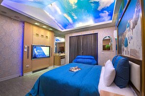 Een hotelkamer met een groot bed, een televisie, een bureau met een computer en een plafondschildering.