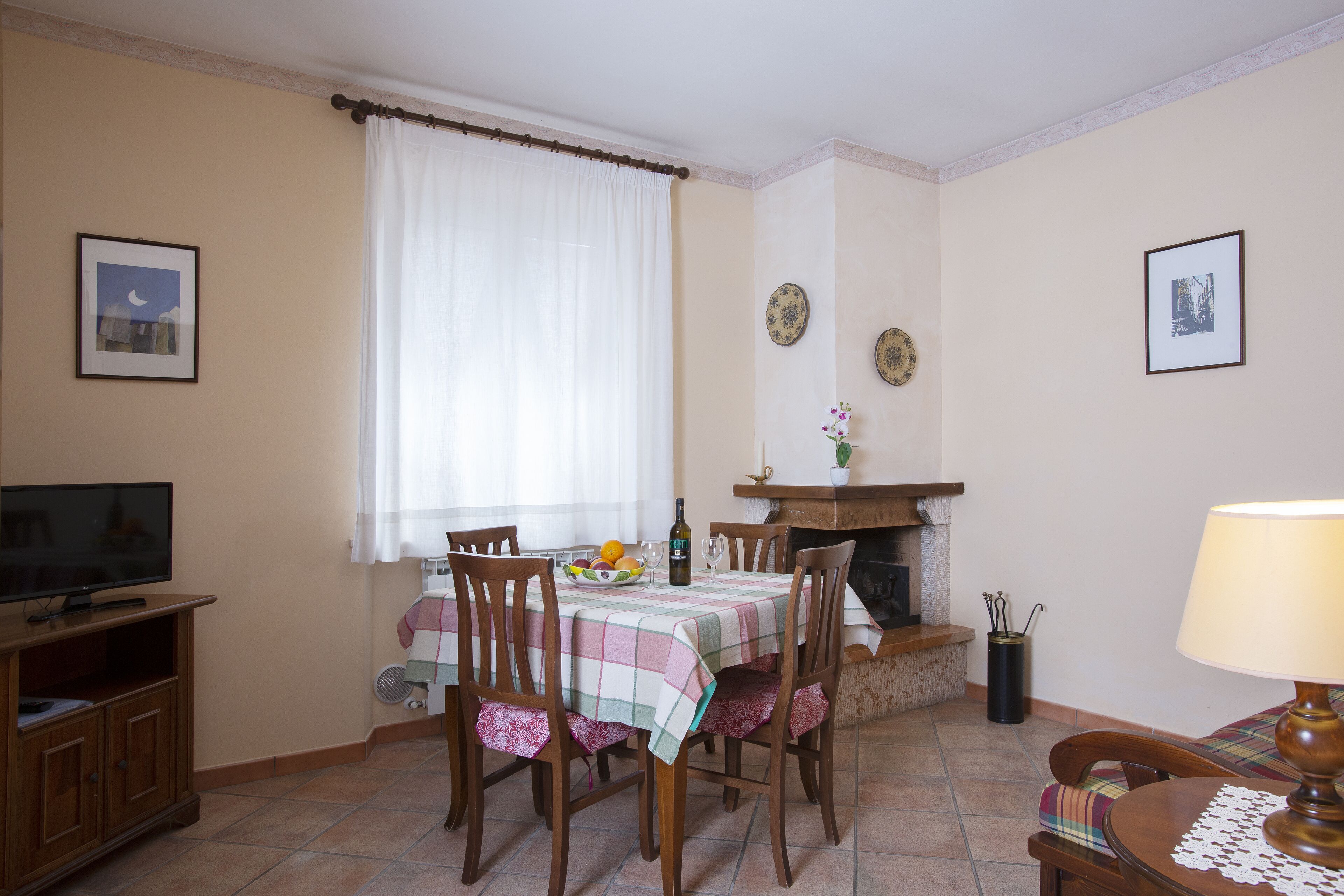 A dining area with a table set for four, chairs, a television, a fireplace, and wall decorations.