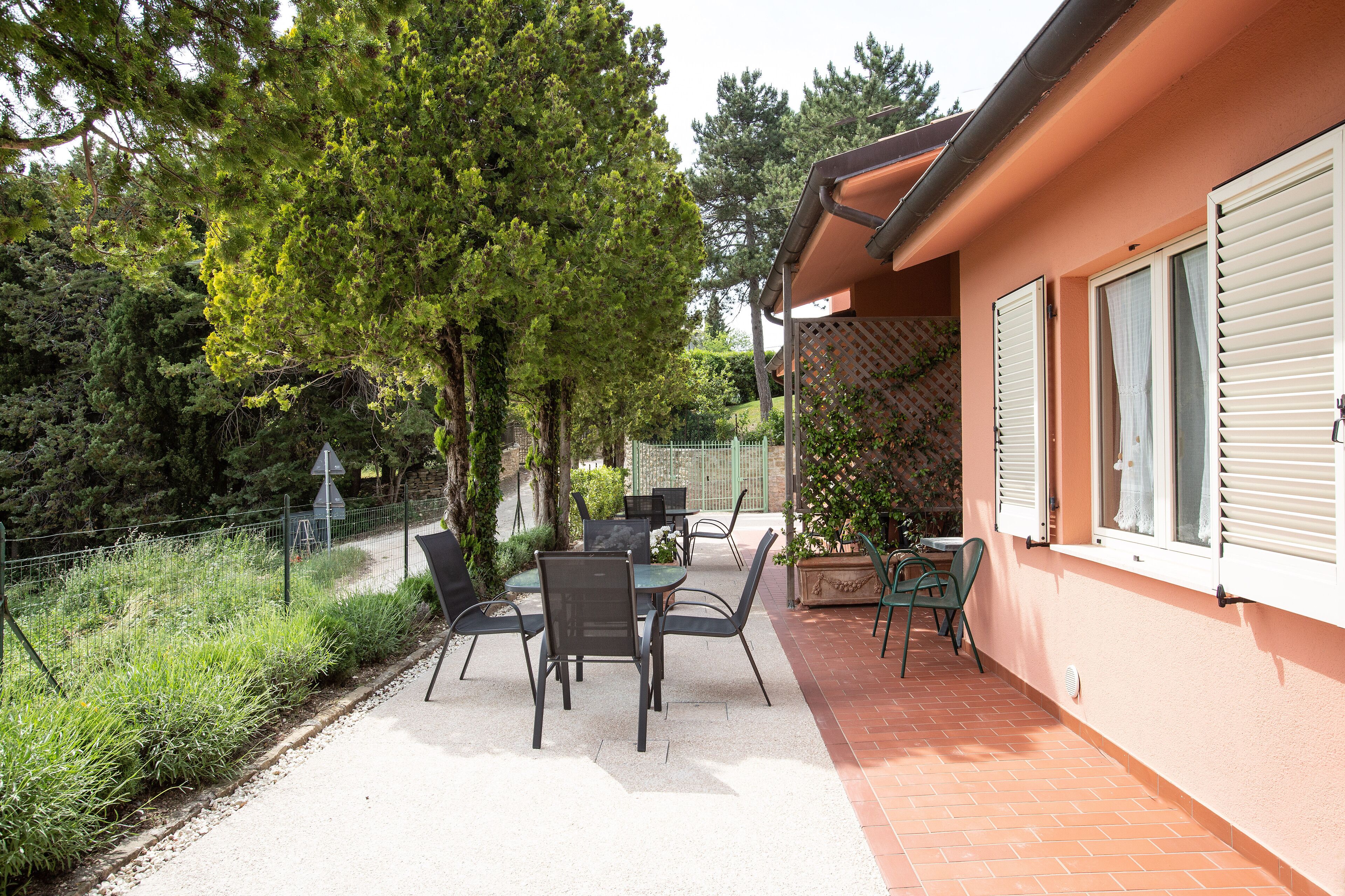 Un patio al aire libre con una mesa y sillas, rodeado de follaje y un edificio con persianas.