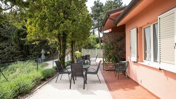 Un patio al aire libre con una mesa y sillas, rodeado de follaje y un edificio con persianas.