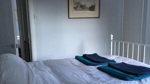 Een net opgemaakt bed met een witte deken en opgevouwen blauwe handdoeken.