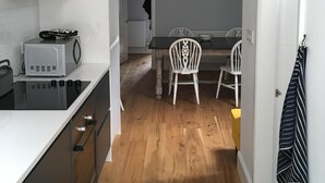Een smalle keuken met een magnetron, fornuis en kastjes. Er is een zithoek met een tafel en stoelen.