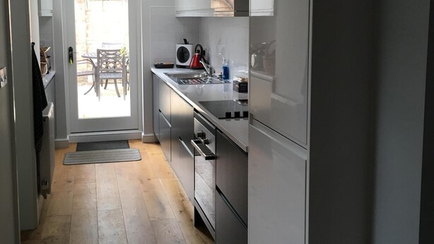 Een moderne keuken met witte kasten, roestvrijstalen apparatuur en een houten vloer.