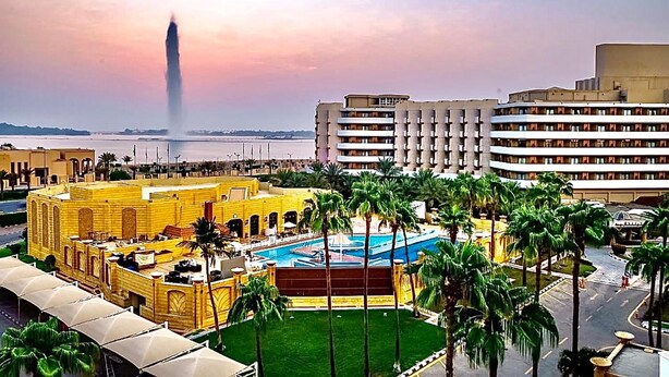 Un hotel con piscina, palmeras y vistas a un edificio alto a lo lejos.