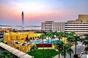 Un hotel con piscina, palmeras y vistas a un edificio alto a lo lejos.