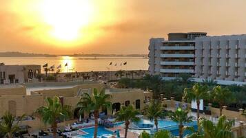 A resort with a pool area, palm trees, and a view of the sunset over a body of water.