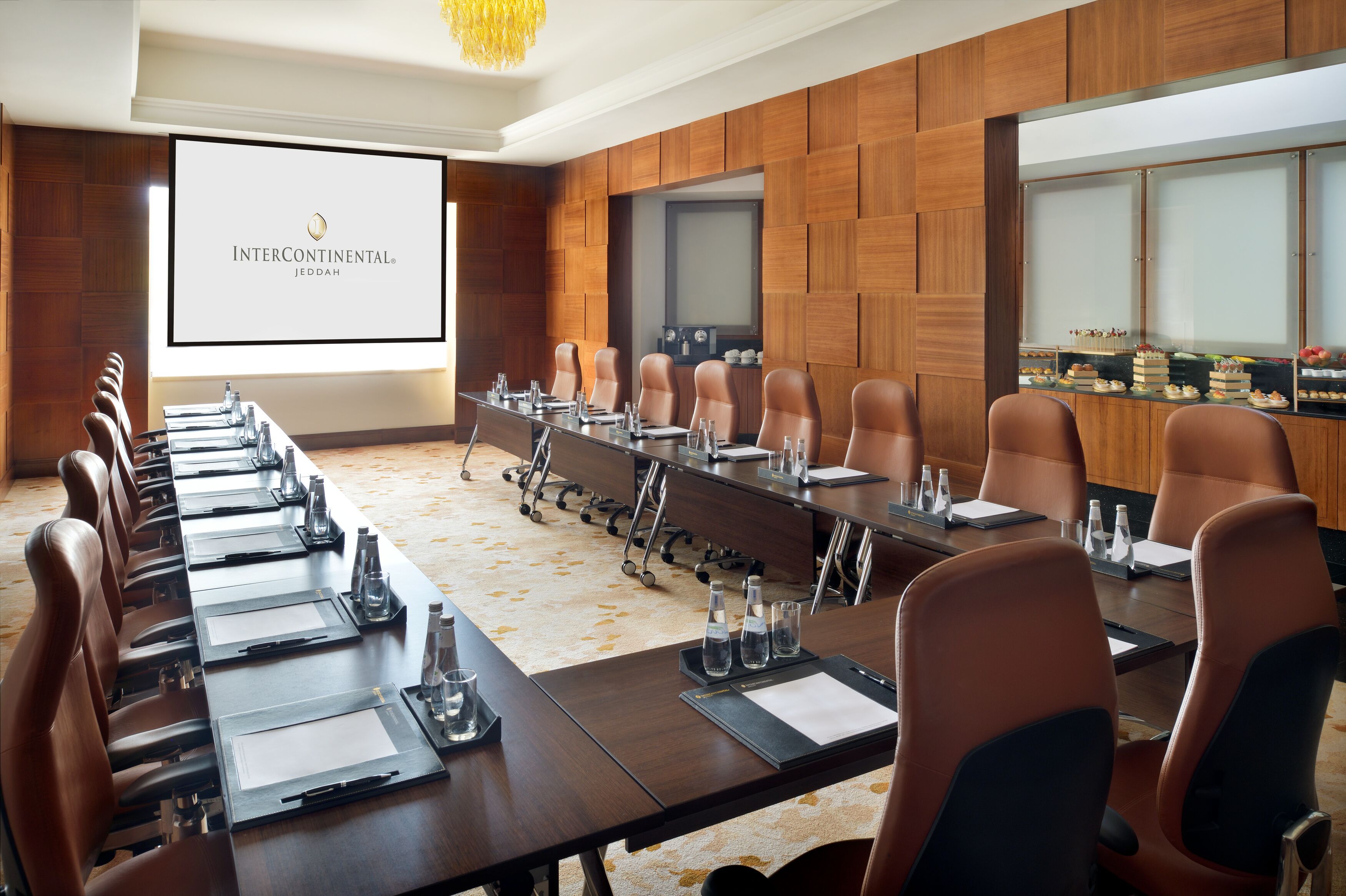 Una sala conferenze con un lungo tavolo, sedie, uno schermo per proiettore e un'area buffet con dolci.