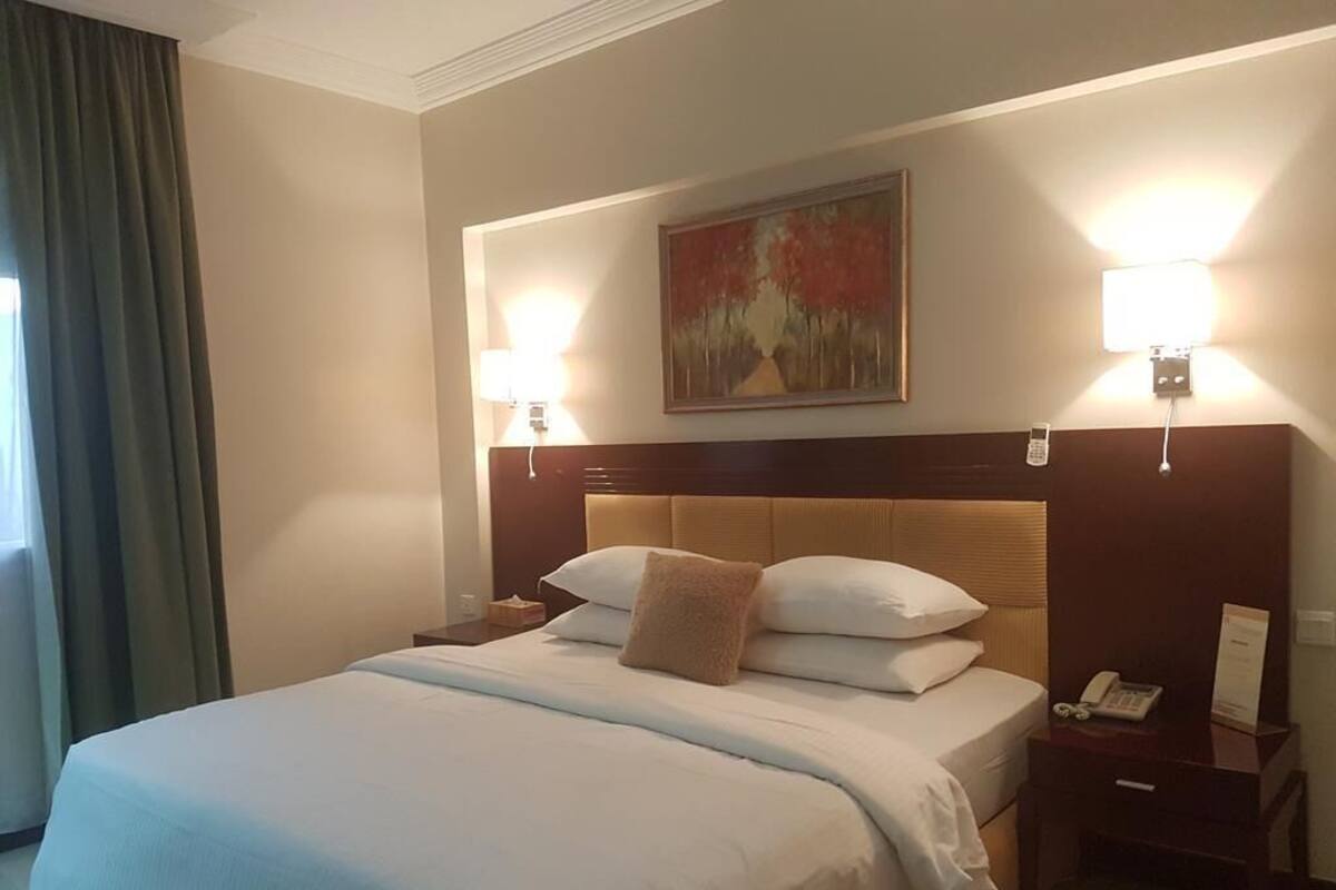 A hotel room with a large bed, two bedside lamps, a painting on the wall, and a telephone on the nightstand.
