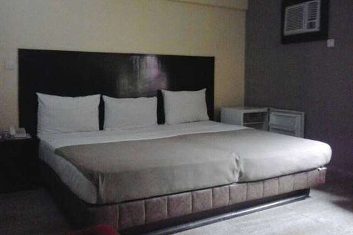 A standard hotel room with a large bed, a nightstand, a bedside table, and a wall-mounted air conditioning unit.