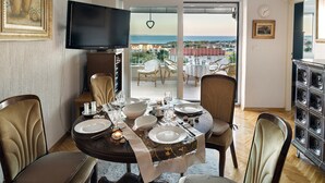 A dining area with a round table set for four, surrounded by upholstered chairs. A television is mounted on the wall above the table.
