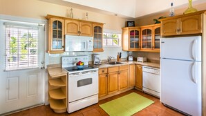 A kitchen with wooden cabinets, a white refrigerator, a stove, and a microwave. - Nautilus Cottage - Charming 7 Mile Beachfront Cottage by Cayman Villas (Seven Mile Beach)