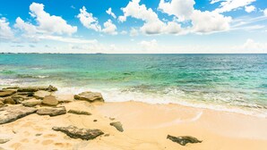 A beach with clear turquoise water, a sandy shore, and scattered rocks. - Nautilus Cottage - Charming 7 Mile Beachfront Cottage by Cayman Villas (Seven Mile Beach)