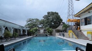 A swimming pool with a tiled deck, surrounded by a building with a staircase and a power line tower in the background. - Rita Lori Hotel Lagos (Lagos)