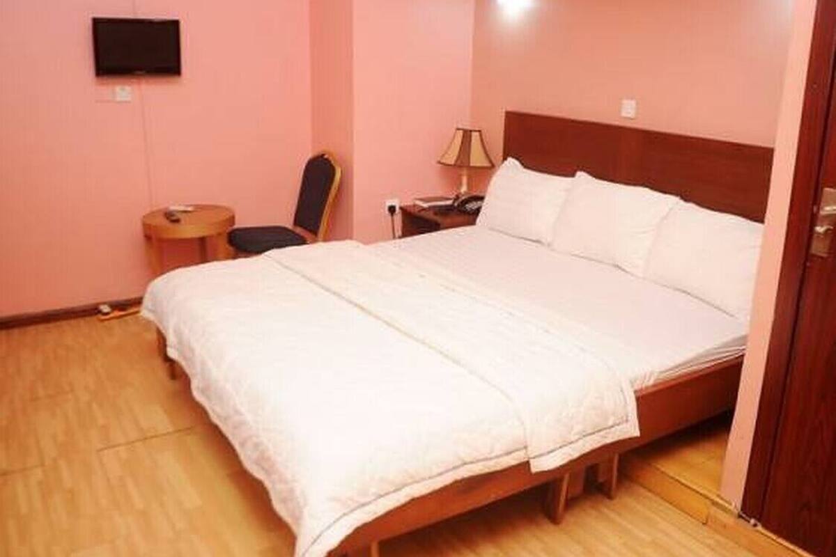 Une chambre à coucher avec un lit, une chaise, une table de chevet et un téléviseur fixé au mur.