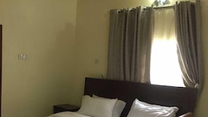 A single bed with a wooden headboard, white bedding, and a nightstand. - Paconsu Suites (Calabar)