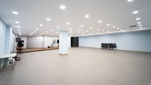 A spacious room with a high ceiling, recessed lighting, a stage area with a podium, and a row of chairs along the wall. - Hotel Navis (Jeju City)