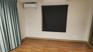 A room with a wooden floor, a black window blind, and a white air conditioning unit. - Hotel Navis (Jeju City)