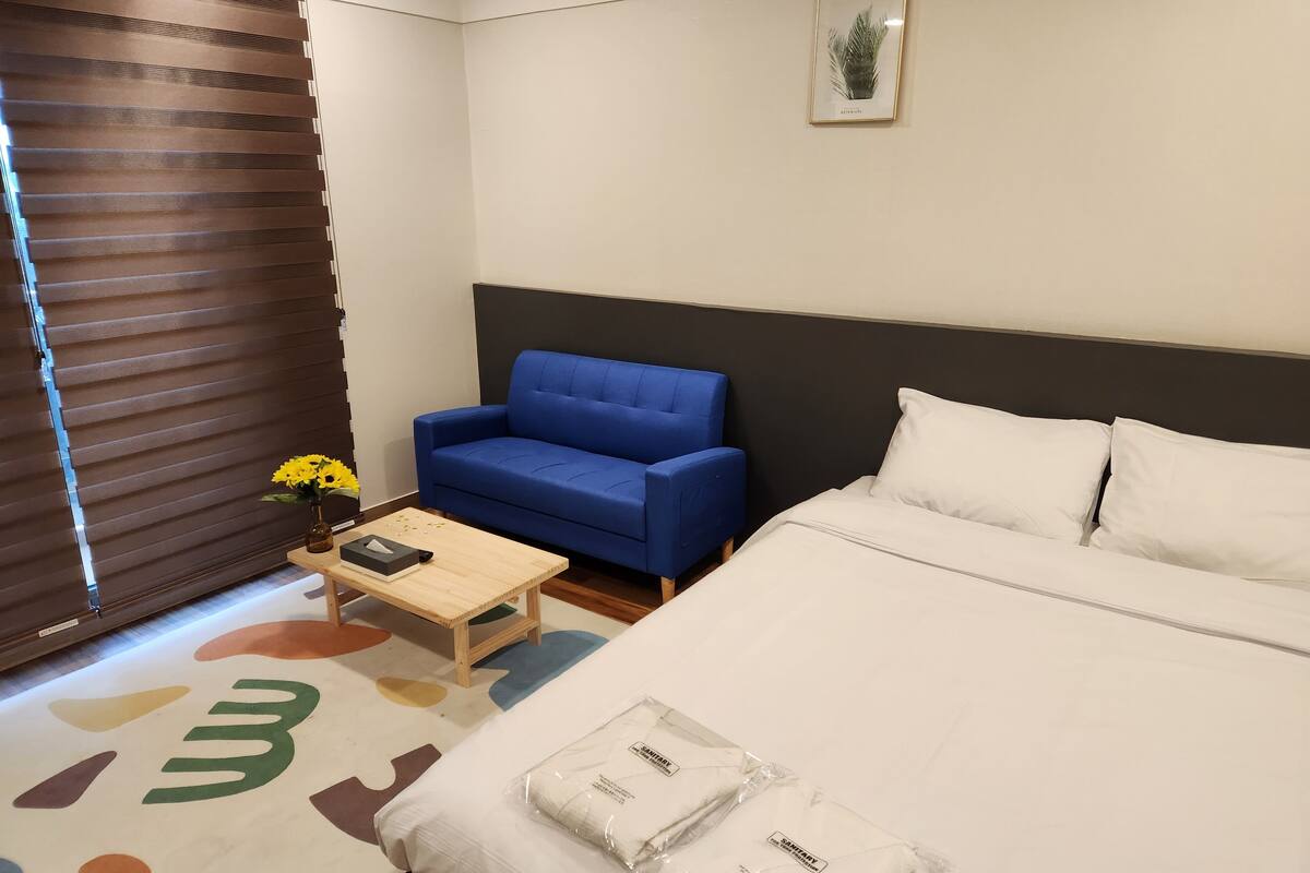 Et hotelværelse med en seng, en blå sofa, et lille bord med en vase blomster og et billede i ramme på væggen.