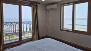 A room with a bed, large windows with a view of the sea, an air conditioning unit, and a balcony with a railing. - Hotel Navis (Jeju City)