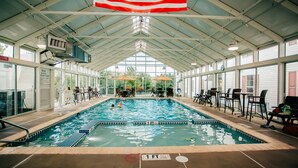 An indoor swimming pool with a covered roof, clear poolside seating, and a view of the outdoors. - The Suites at Hershey - 2 Bedroom (Hershey)