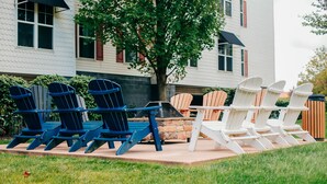 A patio area with Adirondack chairs arranged around a table, a stone fire pit, and a tree. - The Suites at Hershey - 2 Bedroom (Hershey)