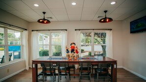A dining area with a long table, six chairs, two pendant lights, and large windows with curtains. - The Suites at Hershey - 2 Bedroom (Hershey)