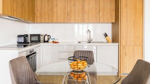 A modern kitchen with white cabinets, a glass dining table, and a fruit bowl. - Staines City Centre by Charles Hope (Staines)