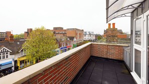 A rooftop terrace with a brick wall, a view of the cityscape, and a building with chimneys. - Staines City Centre by Charles Hope (Staines)