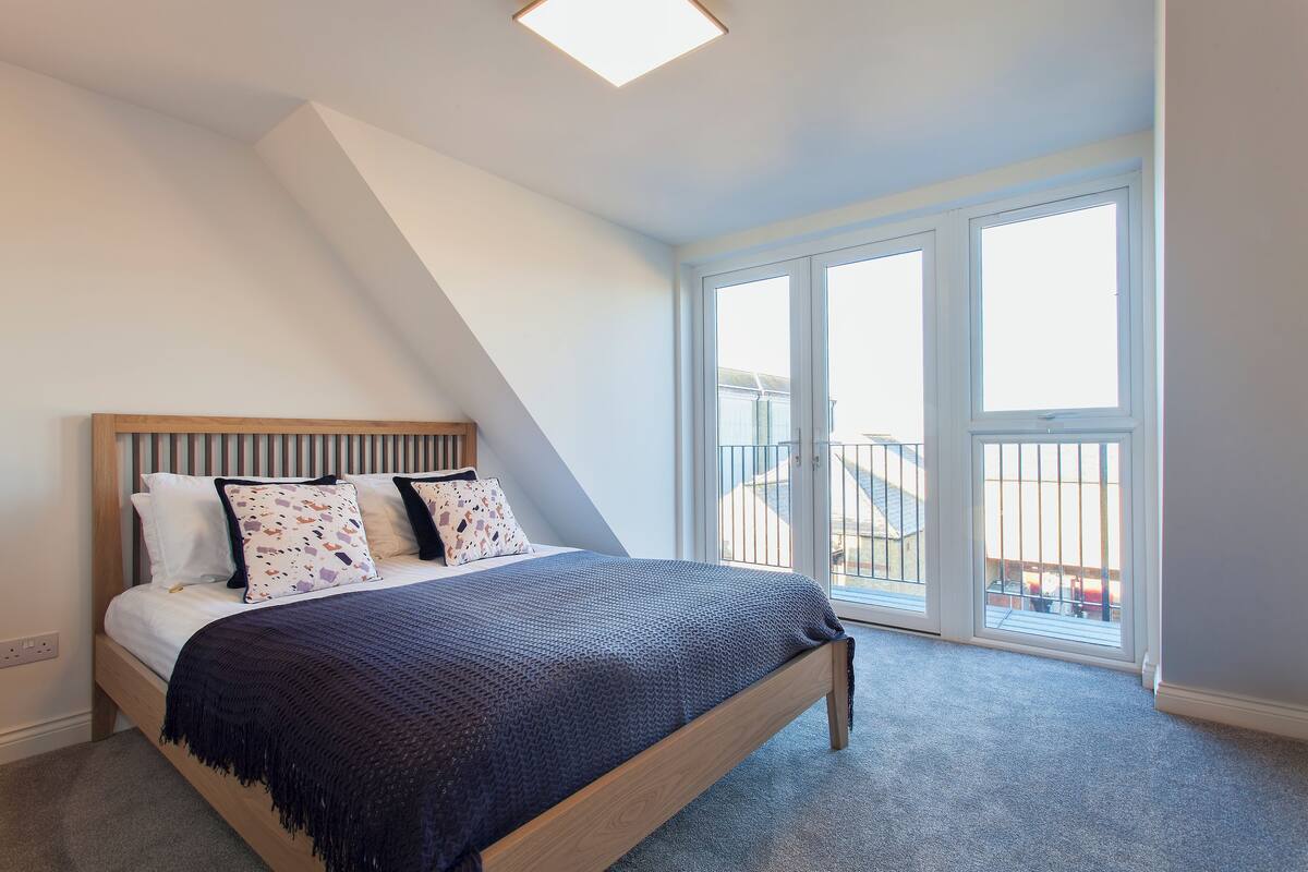 Ein Schlafzimmer mit schrägen Wänden, einem Bett mit Holz Kopfteil und einem großen Fenster mit Blick auf einen Balkon.