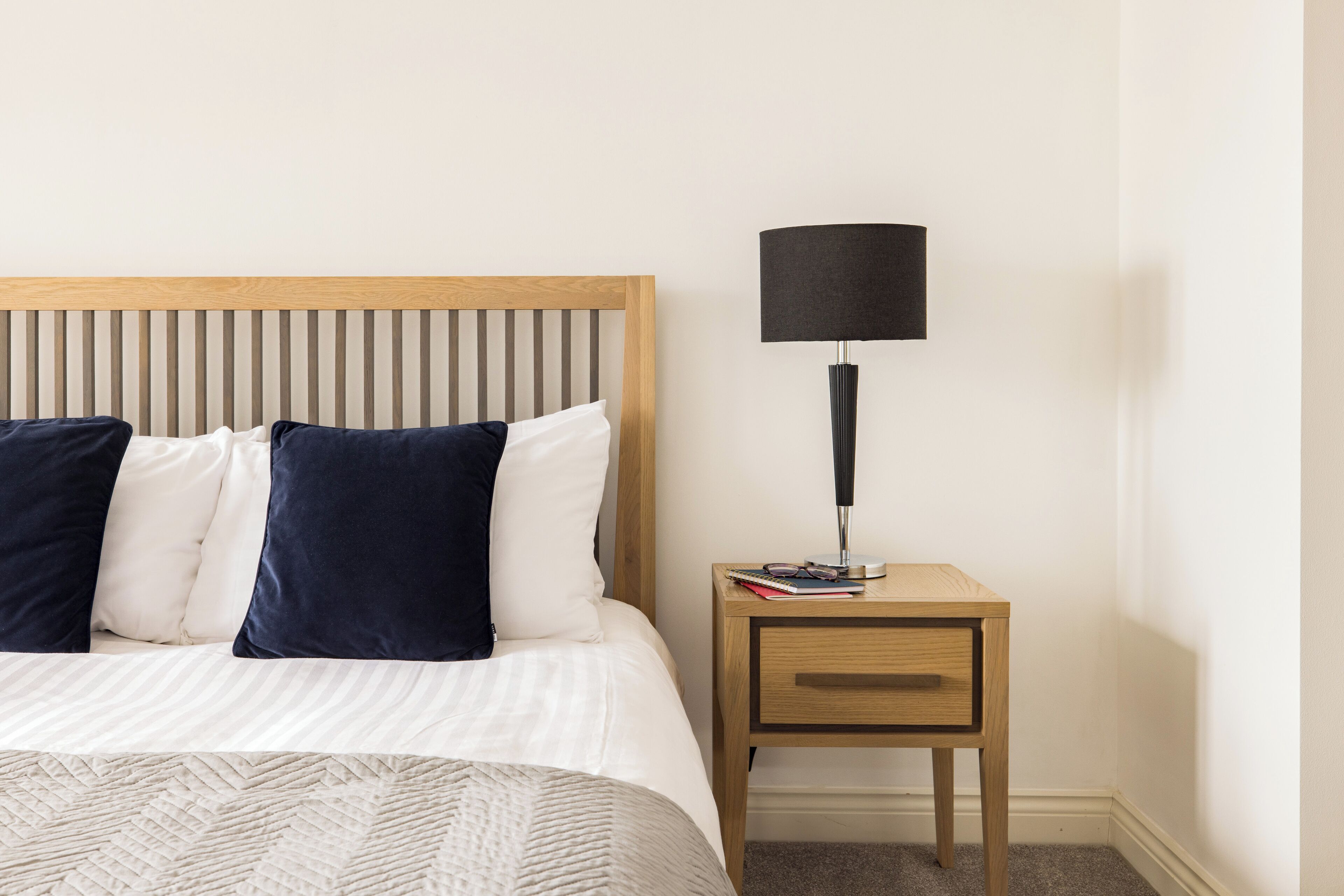 A neatly made bed with a striped headboard, a bedside table with a lamp, and a small drawer.