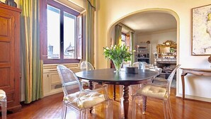 A dining area with a round table, clear chairs, a vase with flowers, and a view through an arched doorway.