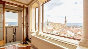 A room with large windows overlooking a cityscape, featuring a view of a historic building with a clock tower.