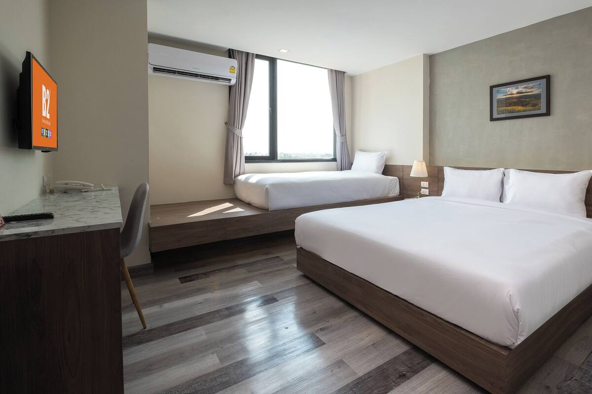 A hotel room with a large bed, a smaller bed, a desk with a phone, and an air conditioning unit.